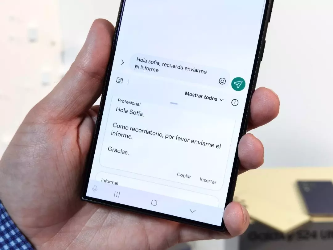 Sobre un Samsung Store podemos ver un Samsung Galaxy S24 Ultra mostrando en pantalla una de las nuevas funciones de Inteligencia Artificial IA. Donde podemos ver el corrector de mensajes para darle un tono profesional.
